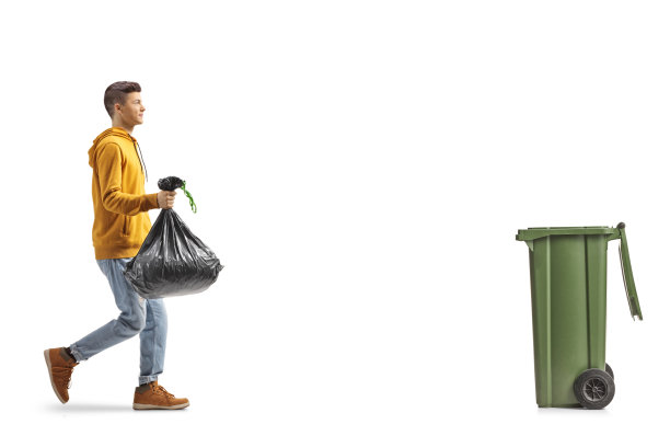 一个人带着一个塑料垃圾袋走向垃圾箱的完整的侧面照片图片下载