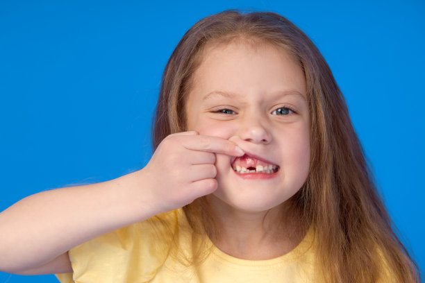 无孩子。可爱的小女孩在蓝色的背景上笑得很开心。第一颗乳牙掉了。儿科牙科与口腔卫生的概念图片下载