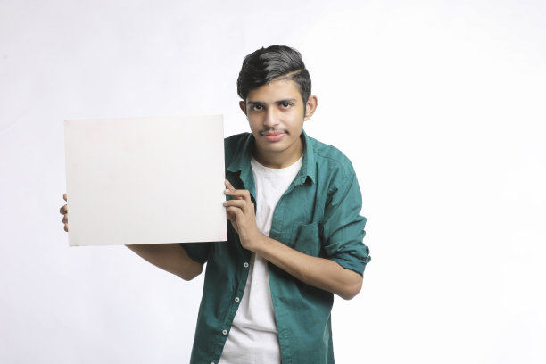 年轻的印度男子在白色背景上展示空白的歌唱板。图片下载