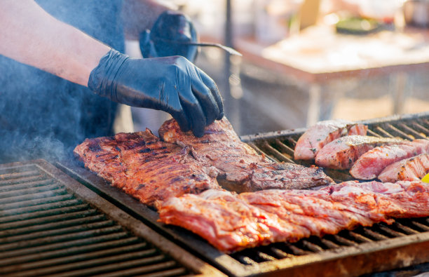 烧烤排骨。戴手套的男子在木炭烤架上翻转烤肋排。全家度假时在后院野餐。烧烤的肉。图片下载