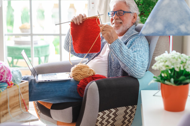 英俊的高级男子正在家里看笔记本电脑上的在线教程，学习如何用毛线编织工作。女性对男性的爱好观念。现代生活方式的人图片下载
