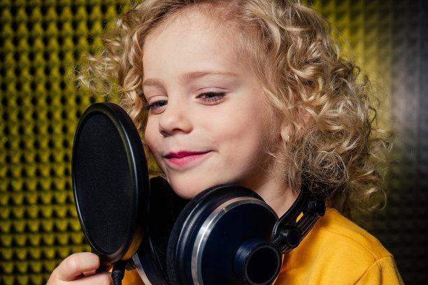 女孩金色卷发风格的明星歌手艺术家在黄色衬衫与耳机录音与麦克风的新歌。图片下载