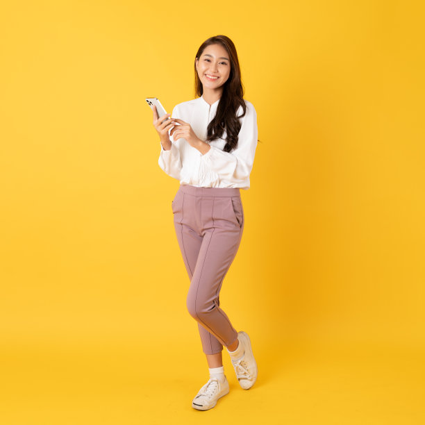 微笑的亚洲女人白色衬衫在黄色的背景使用智能手机与快乐的感觉表示赞赏图片下载