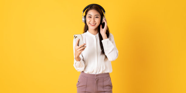 可爱的年轻亚洲少女使用智能手机戴耳机隔离的黄色背景图片下载