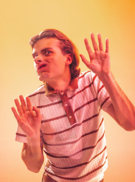 年轻的情感男子的肖像靠在透明的玻璃上，在霓虹灯下的橙色工作室背景上孤立地摆姿势图片下载