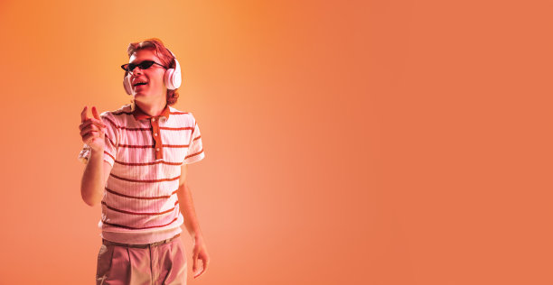 年轻人的肖像听音乐耳机，跳舞孤立在橙色的工作室背景下的霓虹灯。摩天观景轮图片下载