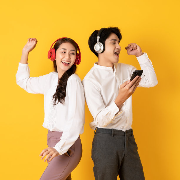 两个年轻漂亮的亚洲夫妇使用智能手机和耳机听音乐隔离在黄色背景图片下载