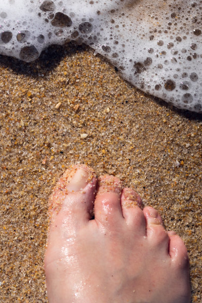 赤脚踩在沙滩和海水的泡沫上图片下载