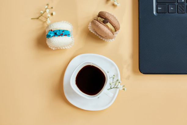 平铺，俯视图办公室桌子书桌，工作空间与笔记本电脑，马卡龙与咖啡杯和鲜花，在橙色的背景，在家工作，远程工作。图片下载