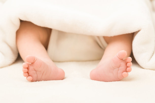 新生儿赤脚躺在床上。脚伸出白色柔软的毯子。宝宝睡觉。特写镜头。图片下载