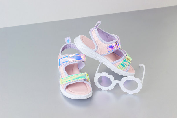 时髦的全息凉鞋为孩子在灰色的背景。闪亮的时尚夏季鞋图片下载