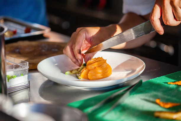 特写厨师的手在酒店或餐厅厨房装饰盘子。准备土豆泥牛排，加入蔬菜，用专用镊子装饰盘子。厨师用手烹饪牛排。图片下载
