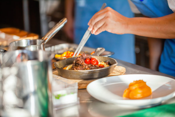 豪华酒店或餐厅厨房装饰盘厨师手特写。准备牛排，装饰菜。现代厨房及厨具图片下载