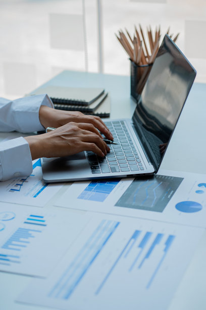 商人拿着笔用财务图工作，笔记本电脑用计算器在办公室分析财务数据，垂直图像。图片下载