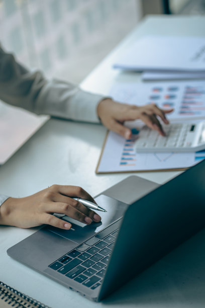 商人拿着笔用财务图工作，笔记本电脑用计算器在办公室分析财务数据，垂直图像。图片下载