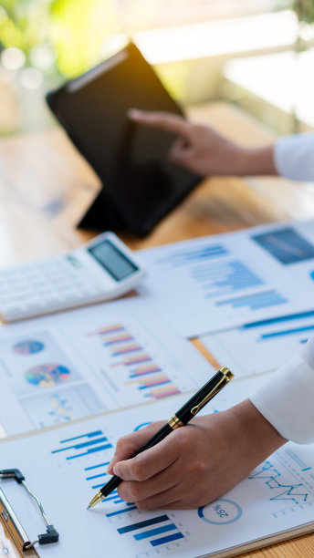 商人拿着笔用财务图工作，笔记本电脑用计算器在办公室分析财务数据，垂直图像。图片下载