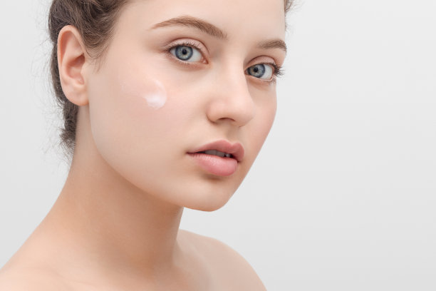 一个美丽的年轻女子的特写镜头与抹面霜在她的脸颊。图片下载