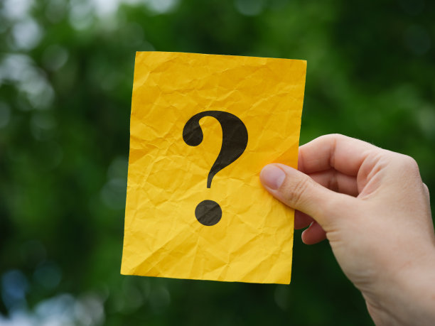 一个女人手里拿着一张黄色的便条纸，上面有一个问号，背景是树叶图片下载