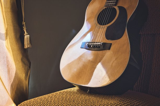 一把西班牙原声古典吉他，有钢弦和尼龙弦放在窗帘旁的椅子上图片下载