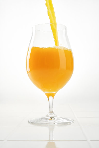 橙汁倒进白色背景的杯子里。浅景深图片下载