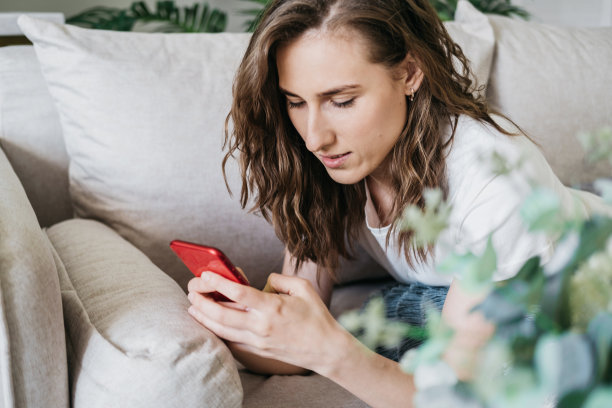 这个女孩手里拿着一个手机。一个女人在互联网上写信息，看图片，搜索信息。女孩为社交网络自拍。女人微笑着坐在家里的沙发上放松图片下载