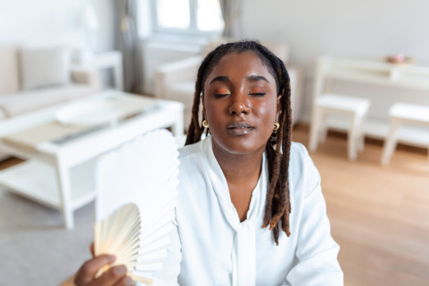 疲惫过热的年轻非洲妇女抱着电风扇受热出汗在家里的笔记本电脑工作室内办公室，烦恼的女孩感到不舒服炎热的夏天天气问题没有空调的概念图片下载