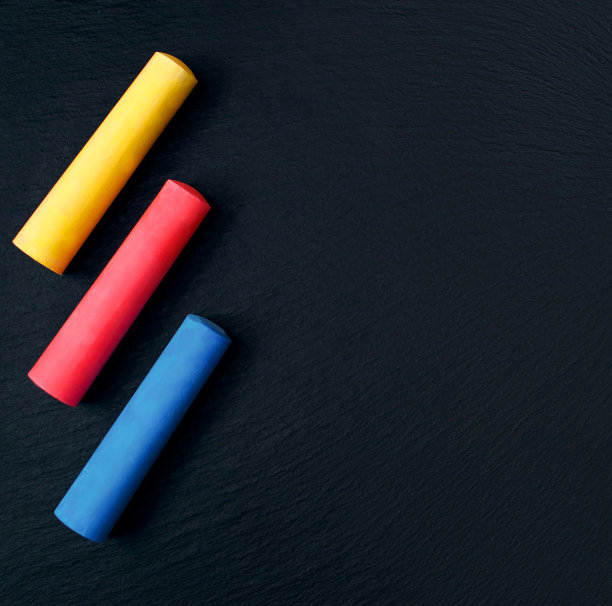 三蜡笔在一个黑色的纹理黑板，黄色，红色和蓝色粉笔，放置文本图片下载