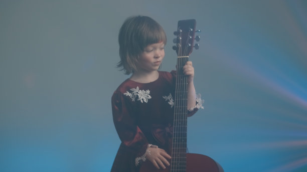 穿着复古礼服的小女孩像弹奏低音提琴一样弹奏着原声吉他图片下载