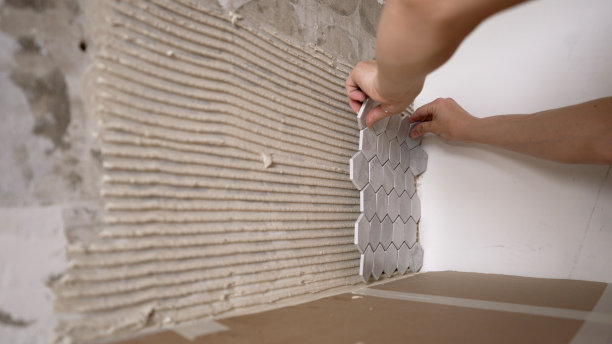 马赛克瓷砖厨房围裙。师傅的手把马赛克瓷砖粘在一起。用大师之手铺设灰色马赛克瓷砖。图片下载