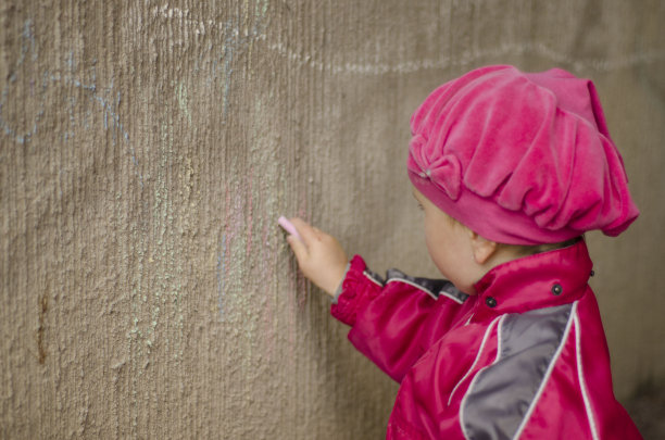 一个白人女孩用粉笔在水泥墙上勤奋地画画。图片下载