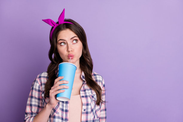 照片肖像的女人喝可乐从塑料杯通过吸管看着空白空间孤立在生动的紫色背景图片下载