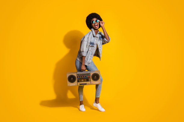 完整的照片甜年轻女子穿休闲牛仔裤衣服抱着音频播放器手臂眼镜孤立的黄色背景图片下载