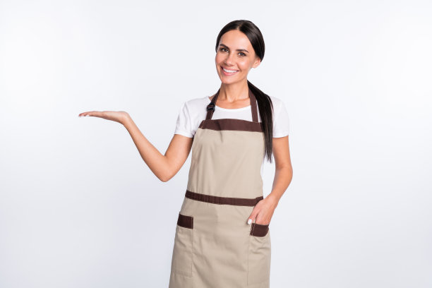 照片乐观漂亮的棕色头发的女士抱空穿t恤围裙孤立在灰色的背景图片下载