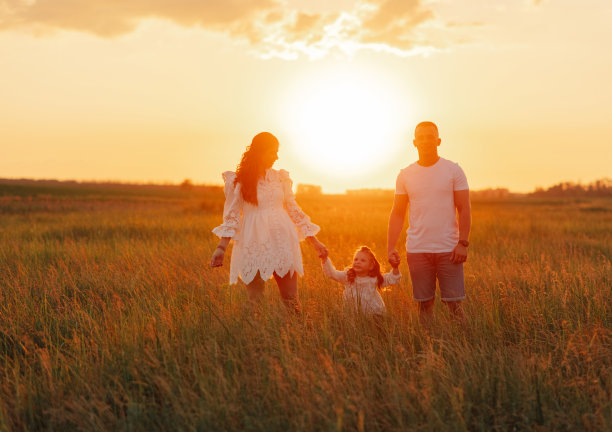 夕阳西下，父母带着女儿在草地上散步。图片下载