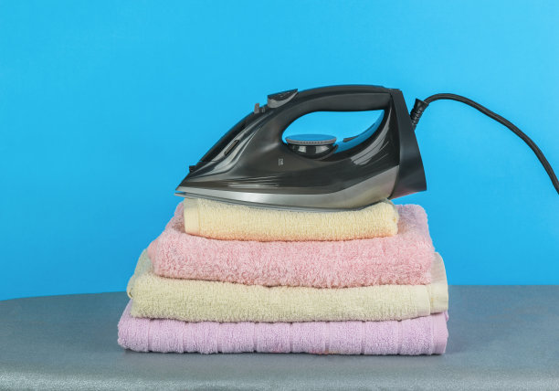 电熨斗放在一堆熨烫过的衣服上，背景是蓝色的。图片下载