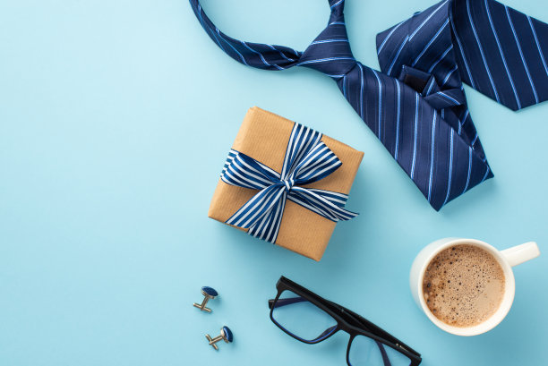 父亲节的概念。顶视图照片的牛皮纸礼品盒丝带蝴蝶结杯咖啡杯袖扣和蓝色领带上孤立的粉彩蓝色背景图片下载