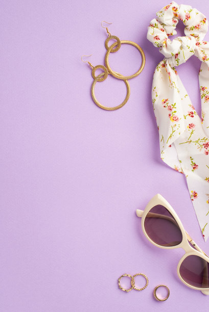 化妆美容概念。俯视图垂直照片的时尚围巾发圈时髦的太阳镜金耳环和戒指上孤立的紫色背景图片下载