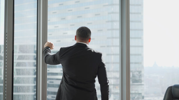 对商人和他的生意来说，这是艰难的时期。他办公室里靠窗的一幅深思熟虑的商人肖像。一个商人站在窗边担心他的生意图片下载