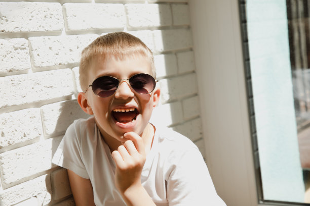 一个戴墨镜的男孩靠在砖墙上笑着图片下载