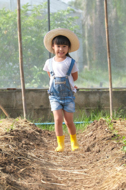 小女孩戴着帽子在花园里帮助她的妈妈，一个小园丁。可爱的女孩在菜园里玩。图片下载