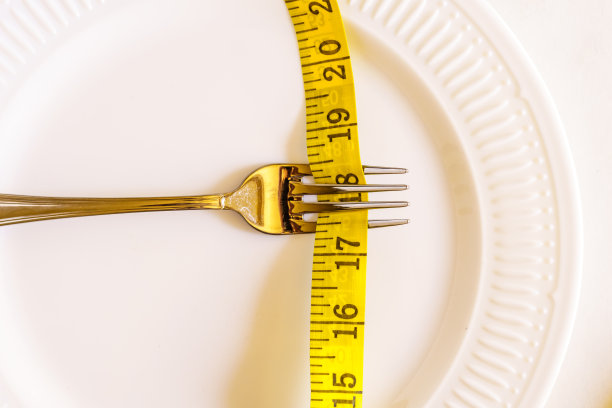 空的白色盘子用叉子夹住卷尺。饮食概念图片下载