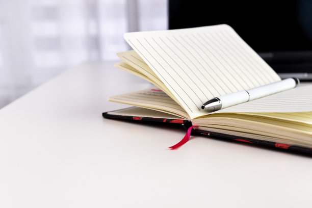 白色办公桌上有开放式笔记本、钢笔、笔记本电脑等办公用品。有选择性的重点。图片下载