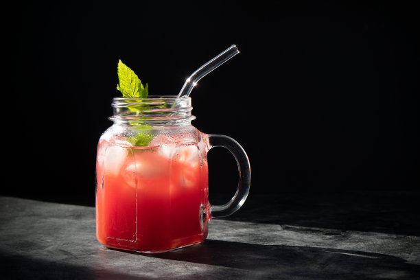 特写新鲜西瓜奶昔与冰和薄荷在罐子与稻草在黑色的背景。暗色低调的照片。有选择性的重点。模糊的背景。图片下载