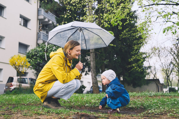 雨中，年轻的母亲带着儿子在公园散步。下雨天，妇女和小孩在小区操场周围探索大自然。图片下载
