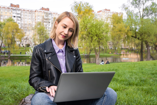 年轻漂亮的女人坐在公园里，拿着笔记本电脑。城市的生活方式。图片下载