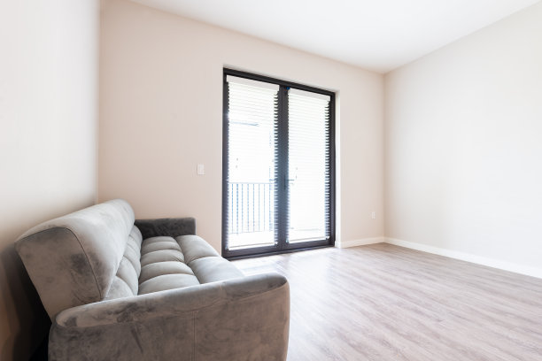 空空如也的客厅内部有蒲团沙发灰色沙发家具在新的现代豪华公寓住宅，大门窗阳台和明亮的自然光线在硬木强化地板图片下载
