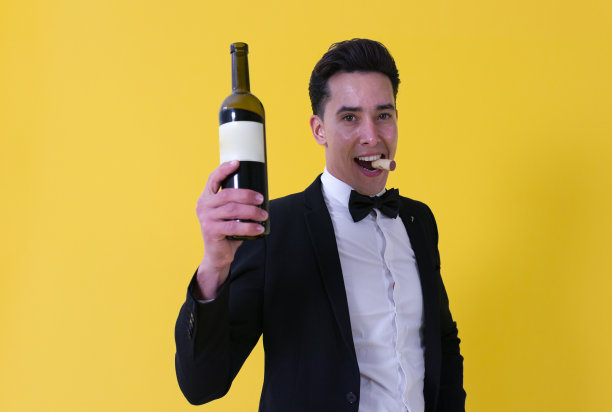 一个衣冠楚楚、面带微笑的男人手里拿着一个打开的白标签酒瓶，嘴里还塞着软木塞图片下载
