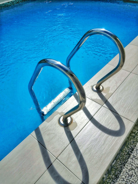 在游泳池边的梯子。蓝水游泳池里的扶手梯子。水池的钢梯。图片下载