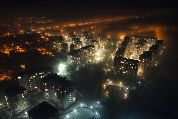 高层公寓大楼和明亮的照明街道在夜晚的城市居民区鸟瞰图。黑暗的城市景观图片下载