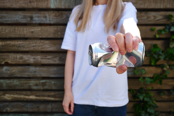 手里拿着皱巴巴的锡罐。可回收的材料。环境保护。“零浪费”。使用饮料容器图片下载